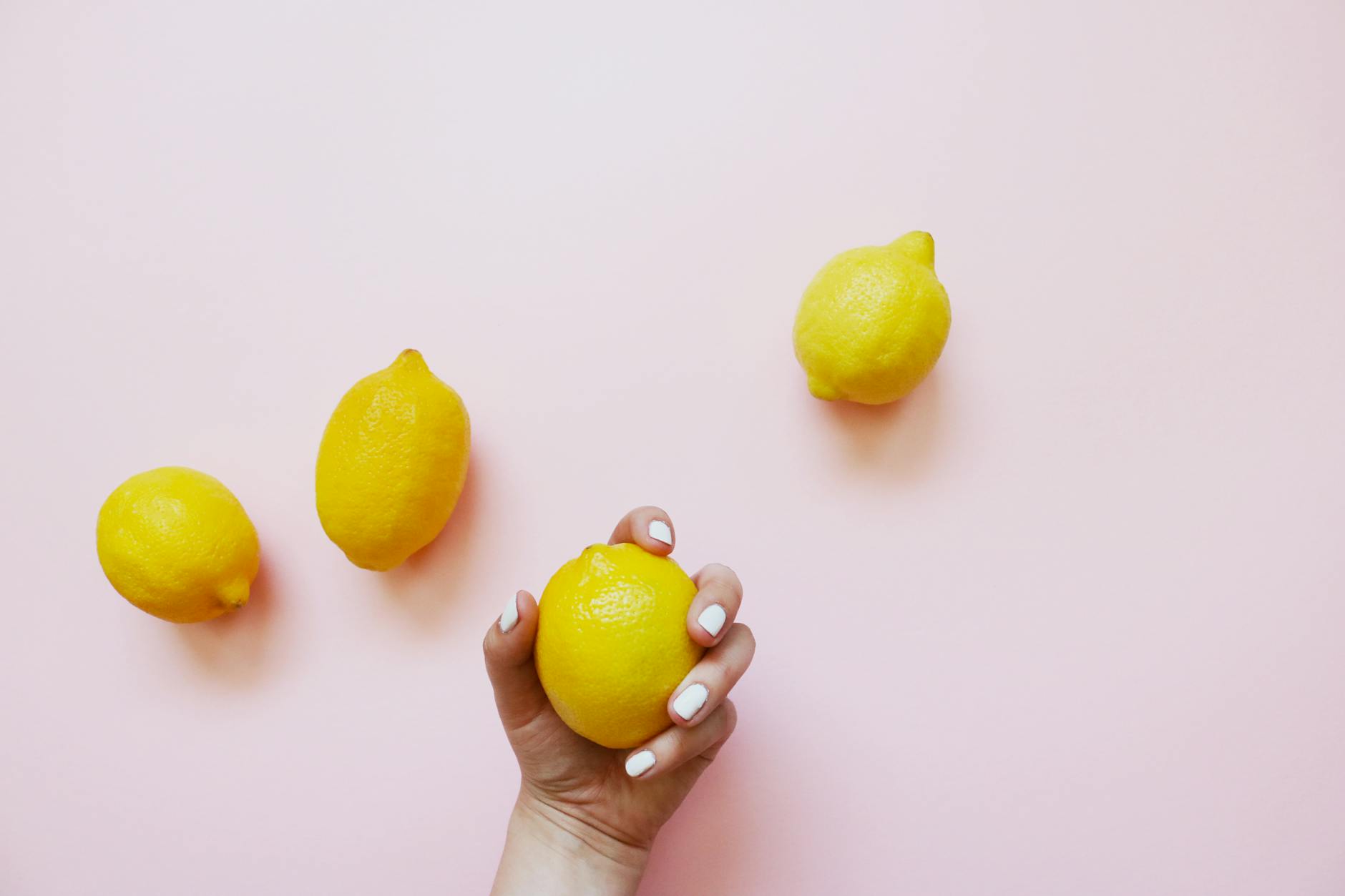 A hand holding a fresh lemon against a soft pink background, symbolizing renewal and arousal recovery