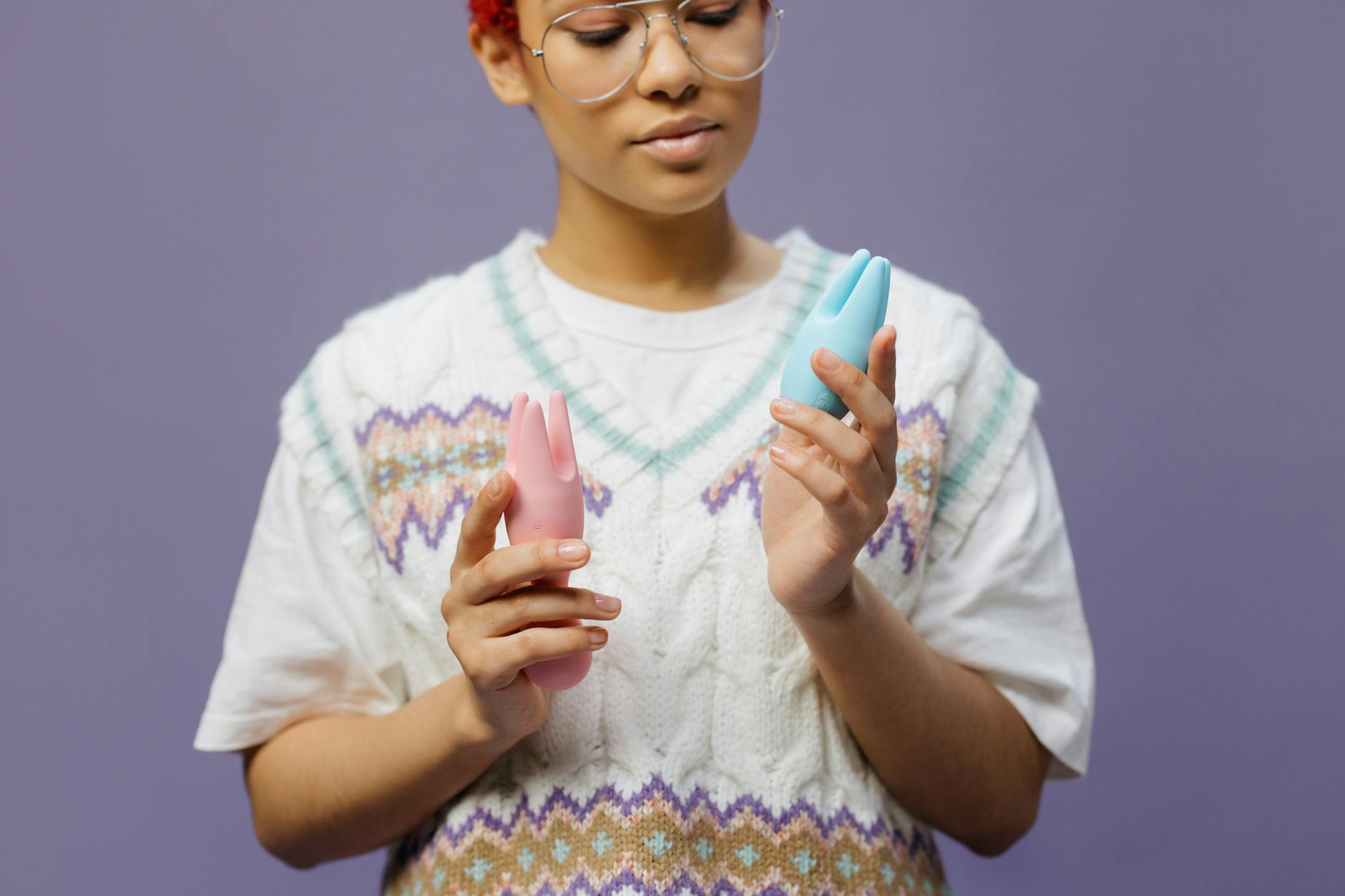 Woman with eyeglasses thoughtfully holding silicone vibrators in both hands